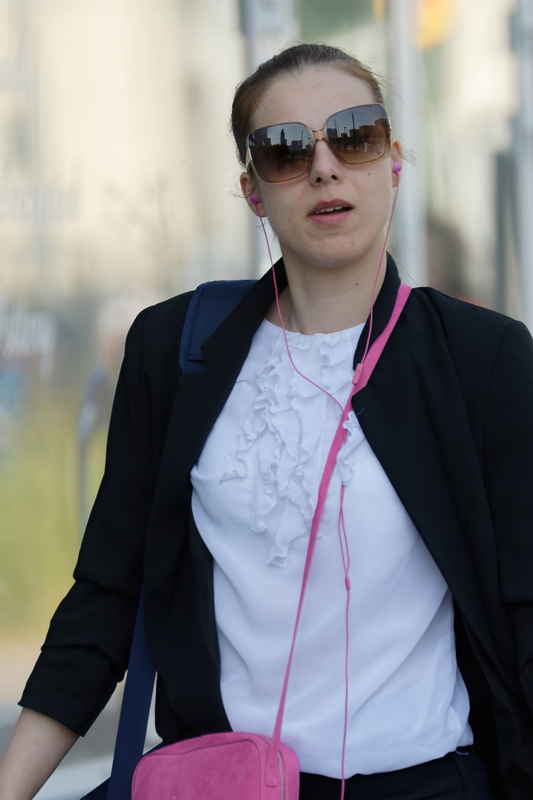 16 - A person wearing a white ruffled blouse under a black blazer with pink earbuds in their ears